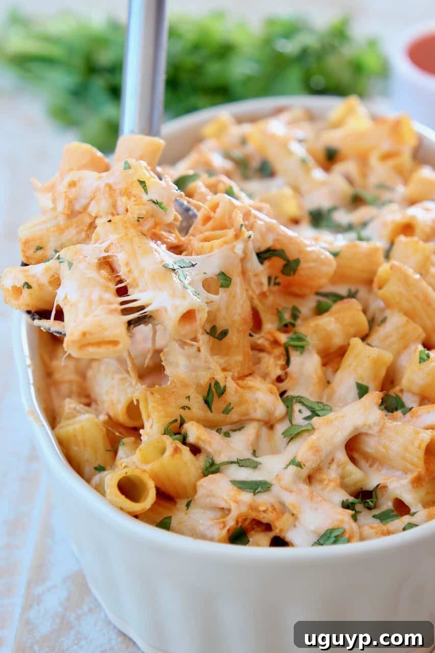Baked cheesy pasta with a spoonful being lifted from the baking dish, showing the stringy mozzarella and rich, creamy sauce. Ideal for family dinners.