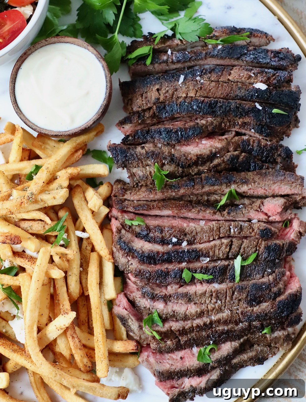 sliced beef shawarma on a platter with crispy french fries and a small bowl of creamy garlic sauce