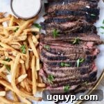 sliced steak on a platter next to french fries and a small bowl of sauce