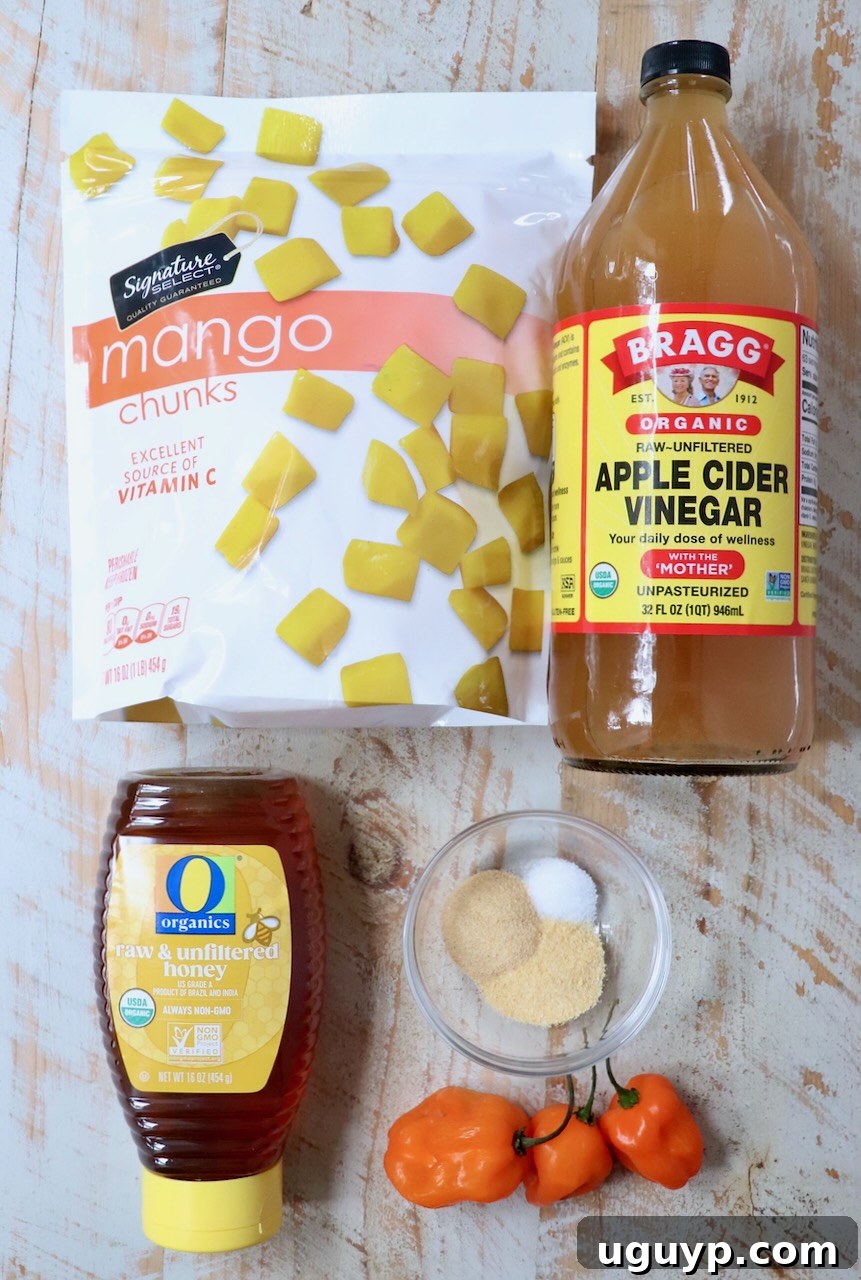 A collection of fresh ingredients for mango habanero sauce, including ripe mango chunks, bright orange habanero peppers, and a small bowl of honey, arranged invitingly on a white wooden board.