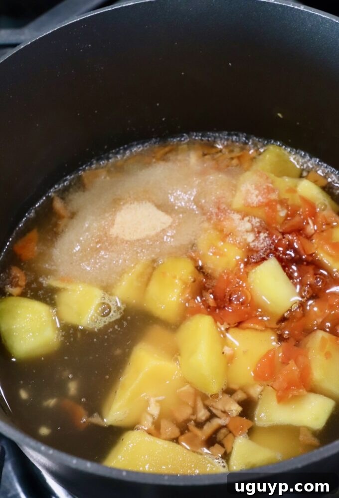 Diced mango chunks, minced habanero peppers, honey, apple cider vinegar, and spices simmering together in a saucepan, beginning to blend their vibrant flavors.
