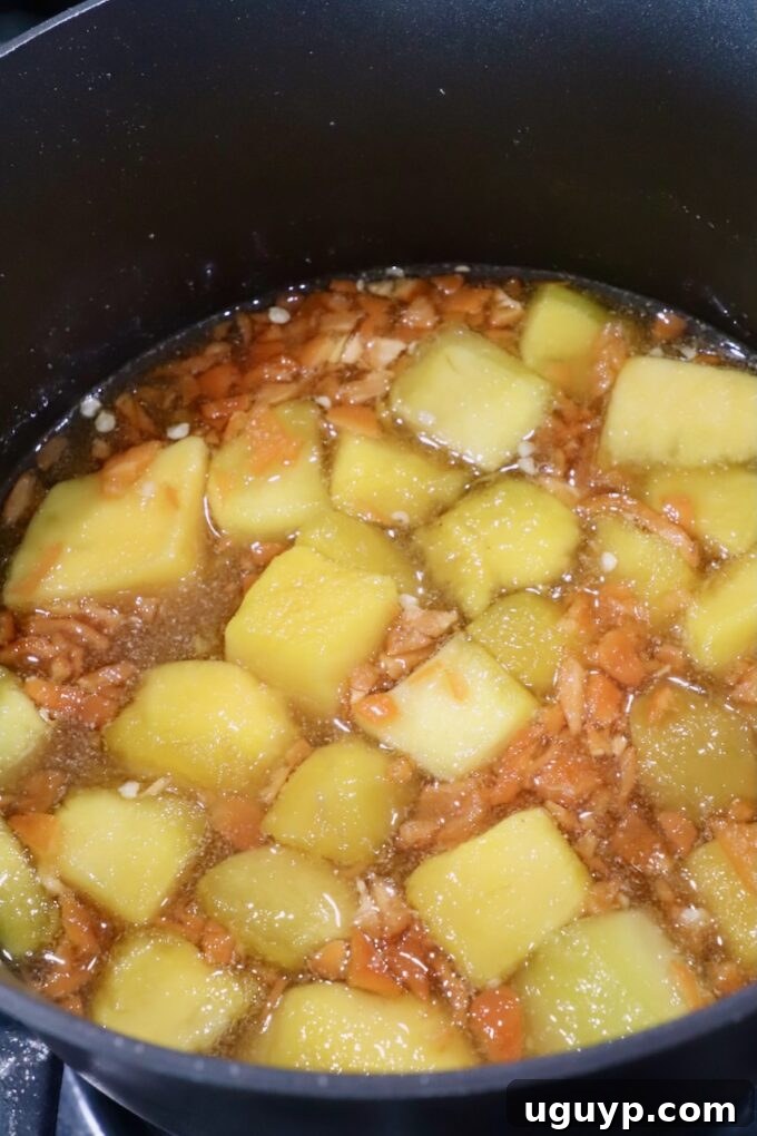 The mango habanero sauce mixture continues to simmer in a saucepan, the mango softening and the liquids reducing slightly, creating a richer, more concentrated base for blending.