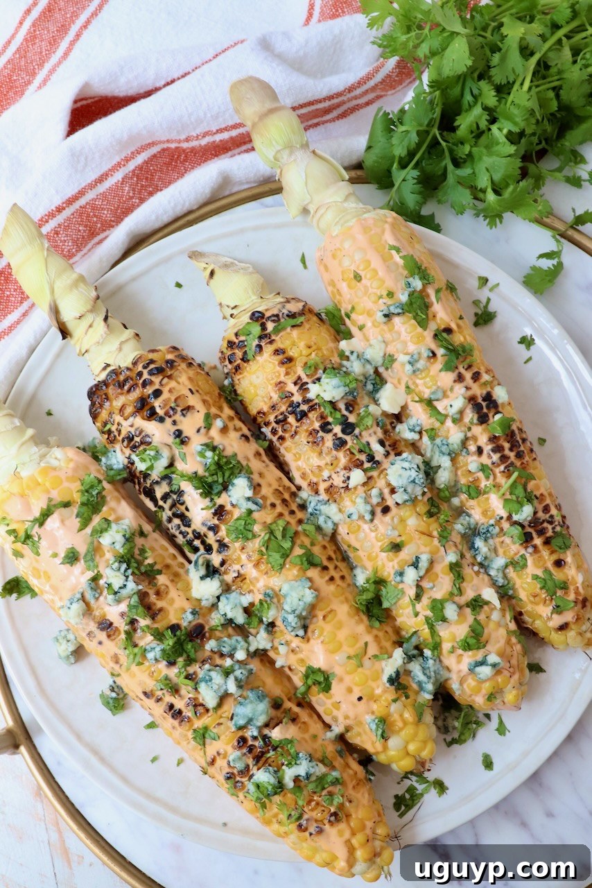 Grilled corn on the cob on a plate, generously topped with blue cheese crumbles and fresh cilantro, ready to be served at a BBQ or game day event.