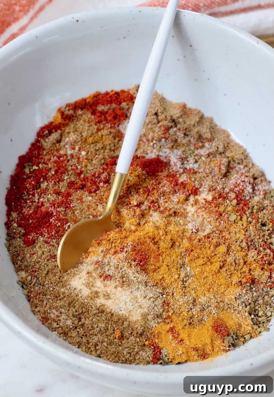 A close-up view of a vibrant blend of Sazon spices mixed together in a bowl with a small wooden spoon, ready to be used.