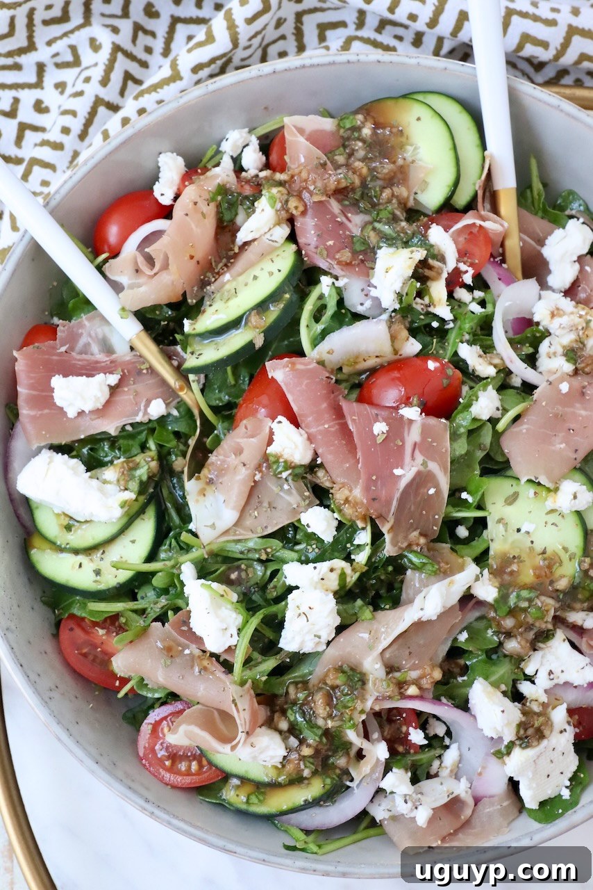 Vibrantly arranged cucumber arugula prosciutto salad in a bowl with tomatoes and feta cheese, ready for serving