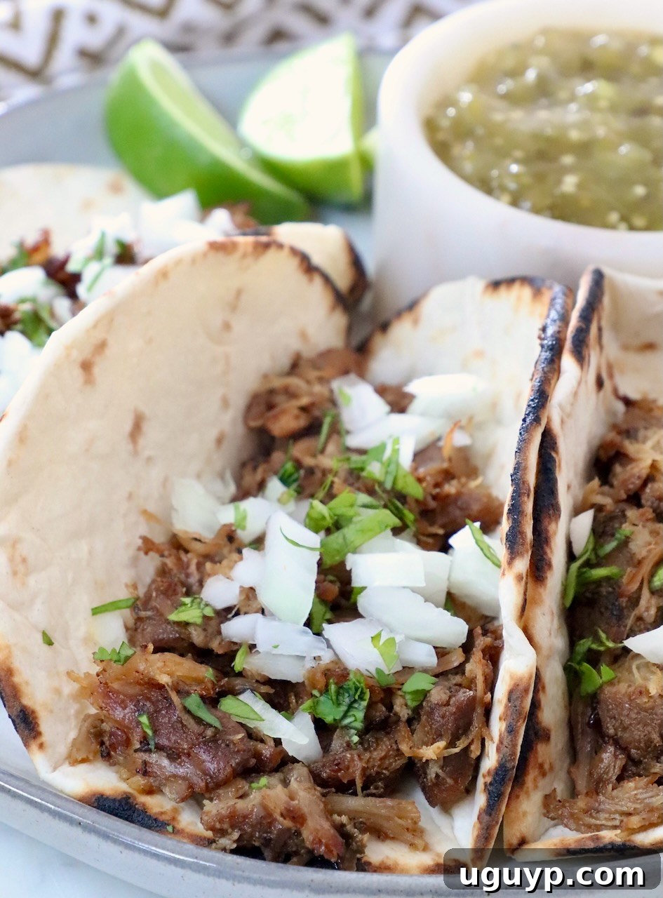 Perfectly shredded pork nestled in warm tortillas, garnished with fresh diced onions and vibrant chopped cilantro, ready to be enjoyed as delicious carnitas tacos.