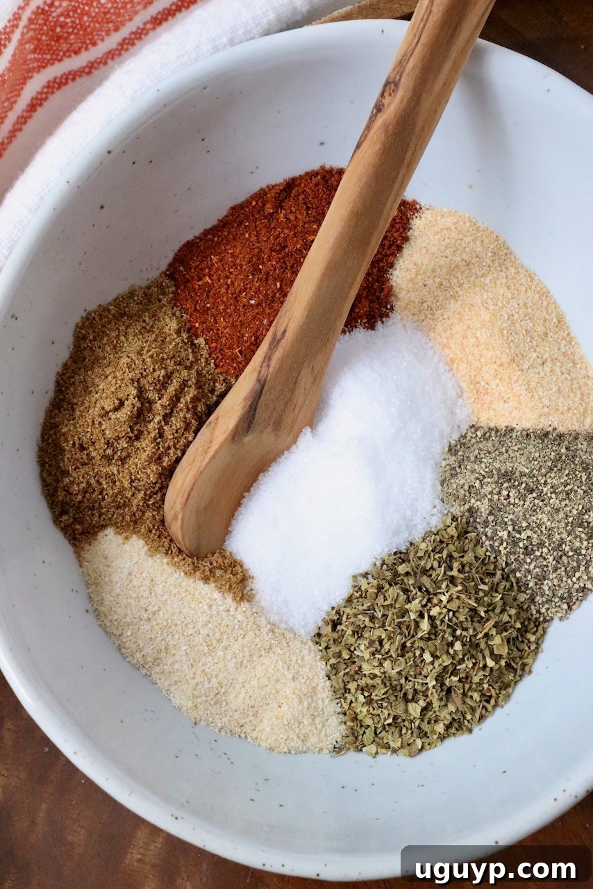 Various dried herbs and spices, elegantly separated in a bowl with a wooden spoon, showcasing the fresh ingredients for the carnitas blend.