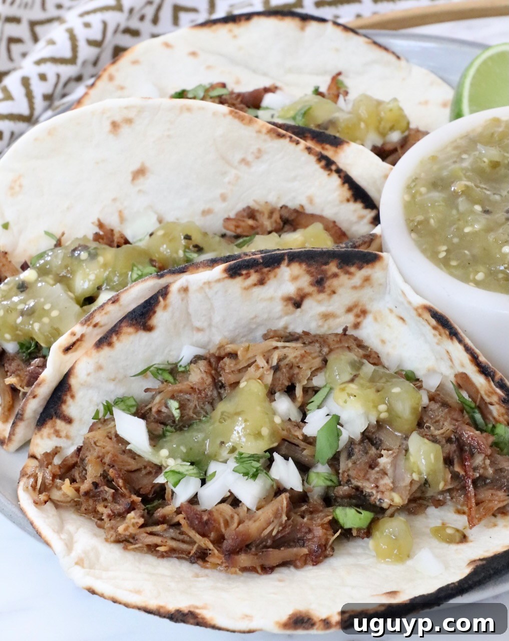 carnitas tacos on a plate with tomatillo salsa on the tacos and in a bowl on the side