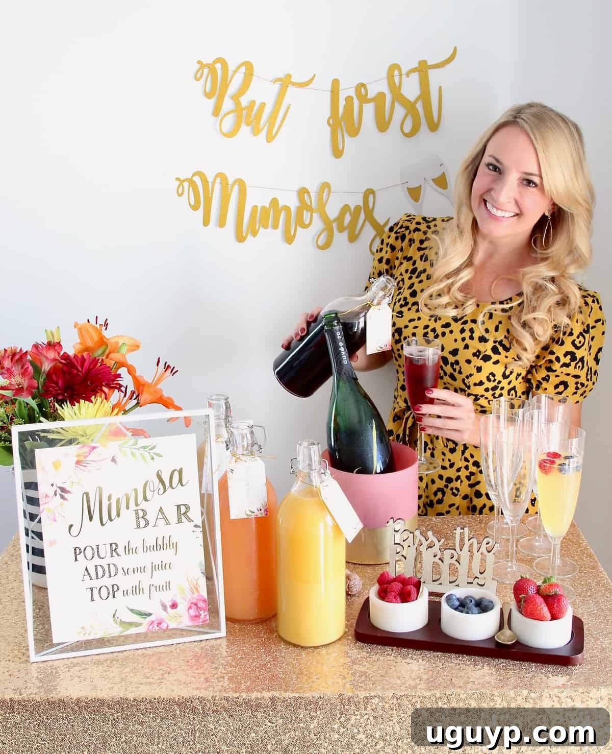 Woman pouring juice into a mimosa standing behind a mimosa bar brimming with fresh ingredients