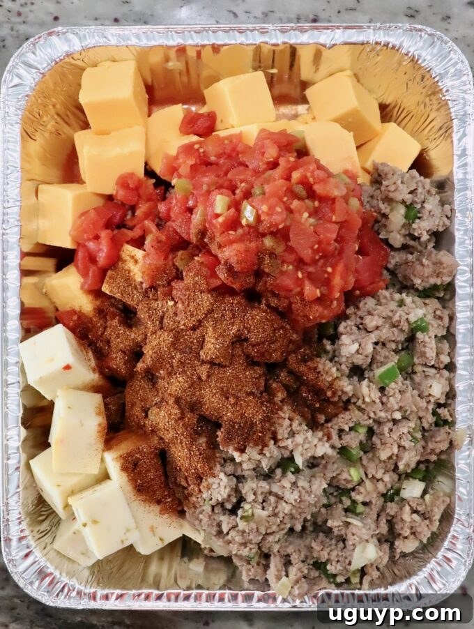 cubes of cheese, cooked, crumbled sausage, diced tomatoes and chili seasoning in an aluminum pan