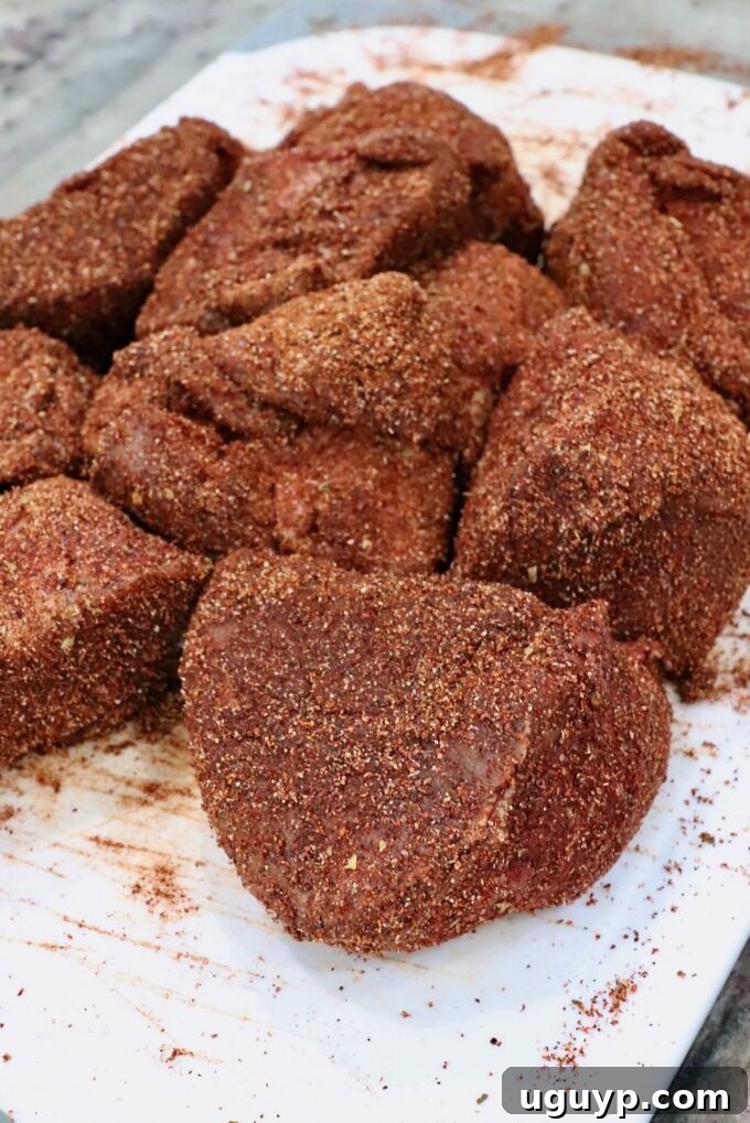 Large chunks of beef chuck roast seasoned generously with birria seasoning, ready for searing.