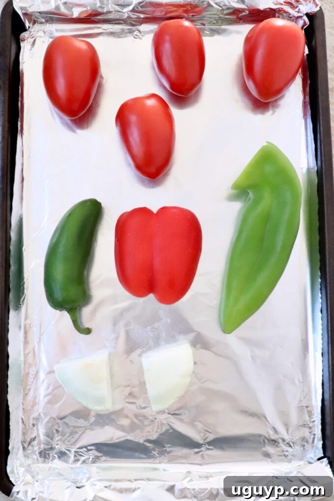 roma tomatoes, peppers and onions on a foil lined baking sheet, ready for roasting
