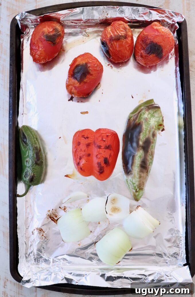 roasted roma tomatoes, peppers and onions on a foil lined baking sheet after broiling, showing charred skins