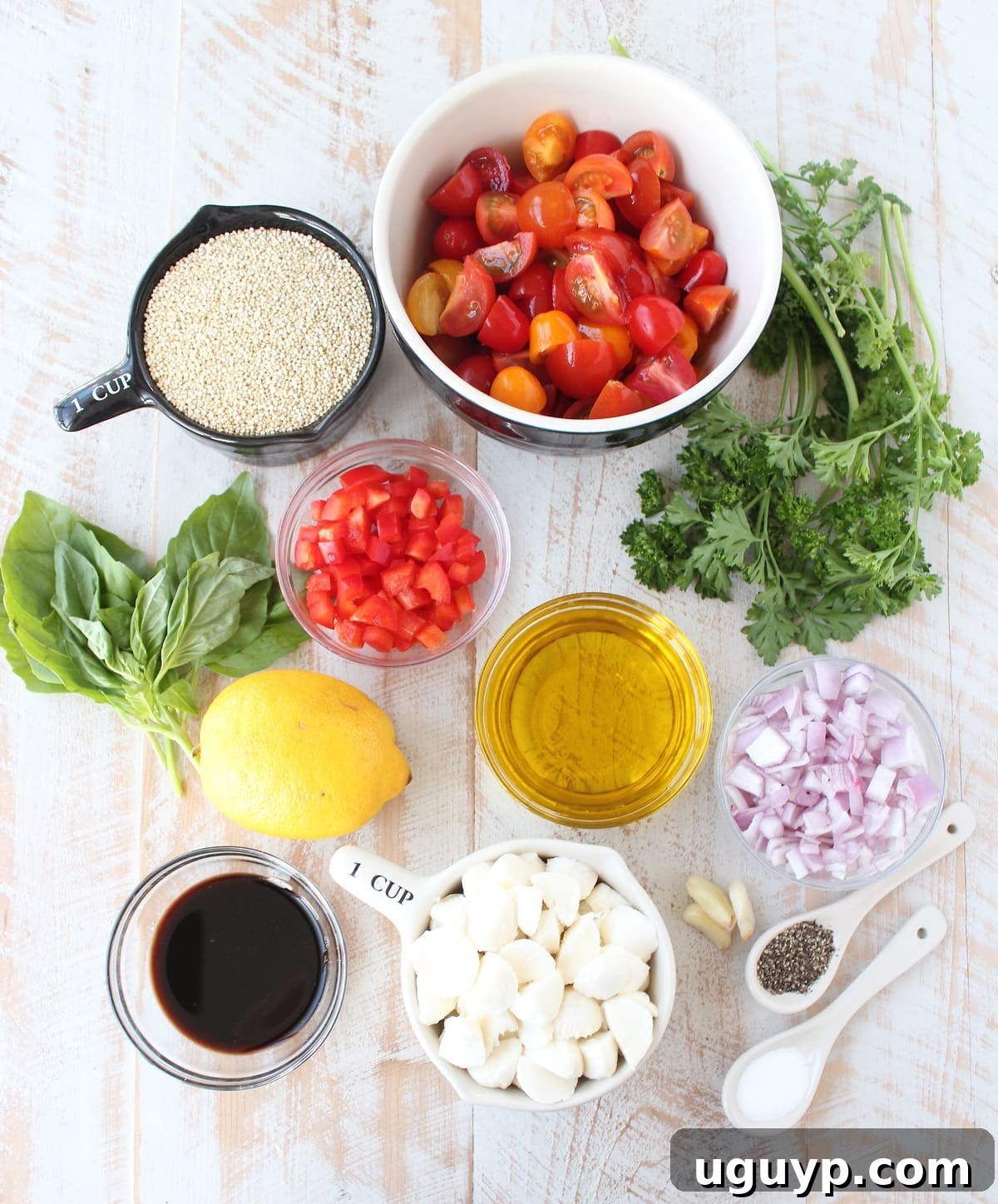 Fresh ingredients for Quinoa Caprese Salad, including quinoa, cherry tomatoes, mozzarella, and herbs, displayed in bowls on a wooden surface.