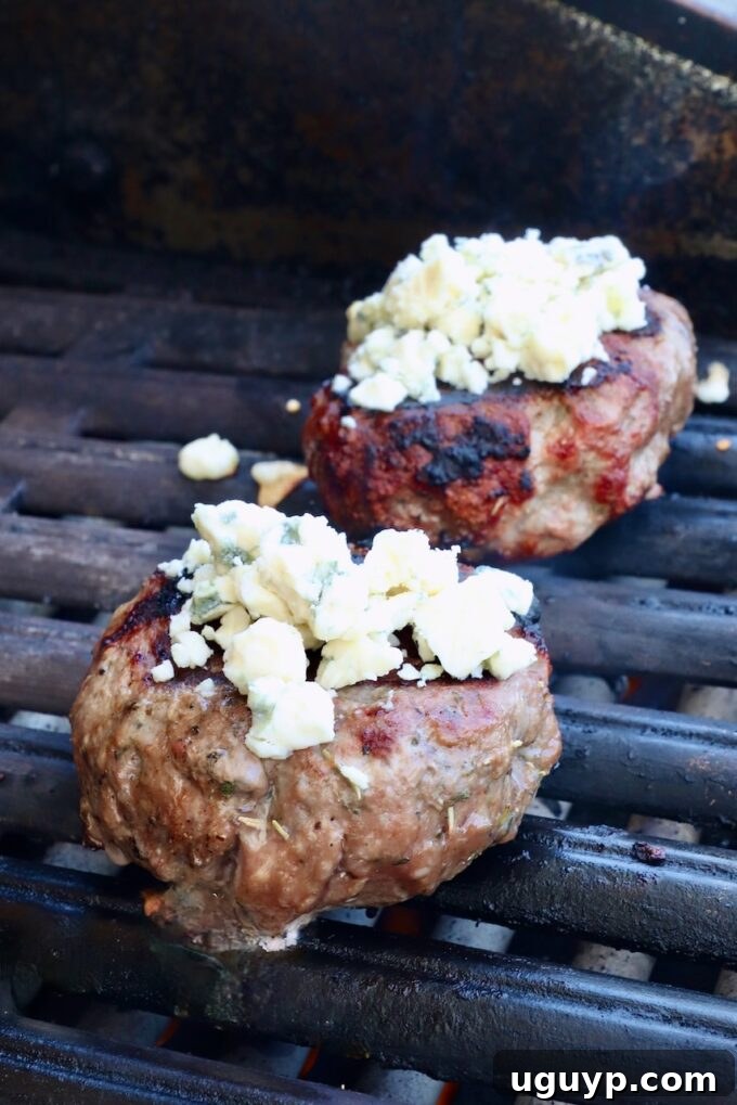 cooked lamb burger patties on a grill topped with blue cheese crumbles