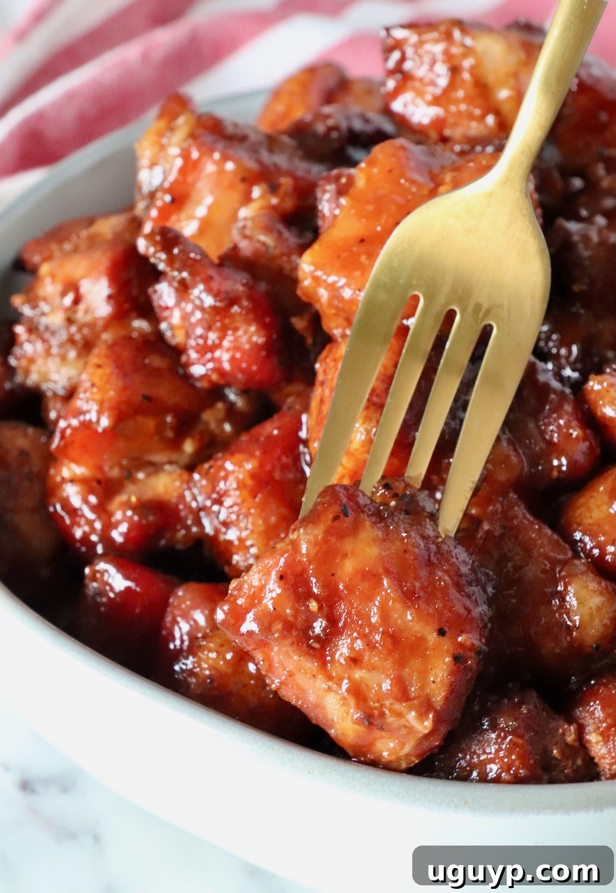 Glazed cubes of smoked pork belly in a bowl, with one piece on a gold fork.