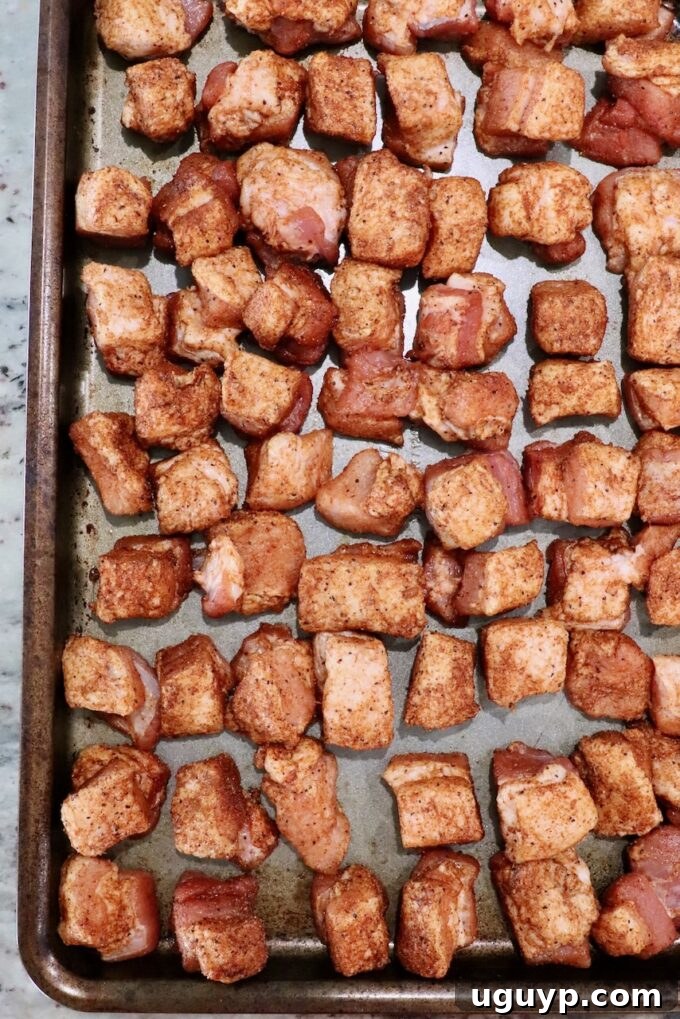 Seasoned cubes of raw pork belly on a metal baking sheet.