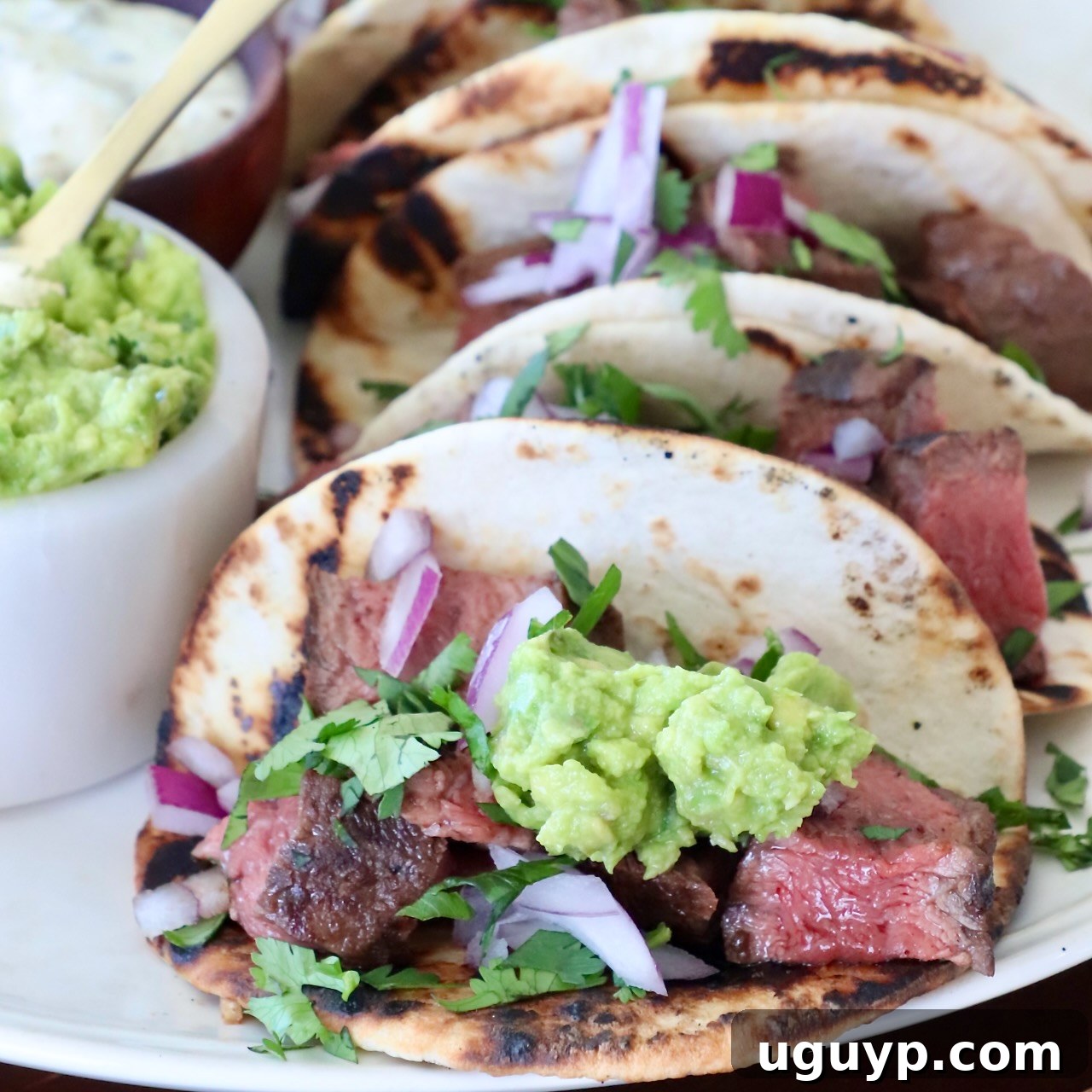 Two vibrant steak tacos, generously topped with fresh guacamole, arranged enticingly on a plate, promising a burst of flavor.