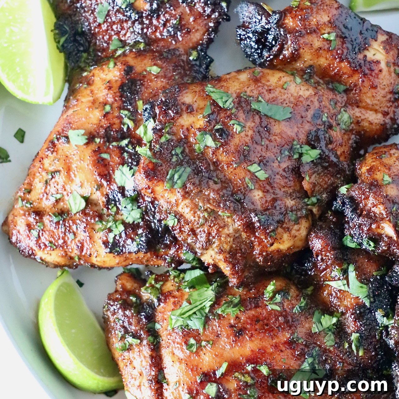 Grilled chicken thighs stacked up on a plate with fresh cilantro and lime wedges, glistening with chipotle honey glaze.