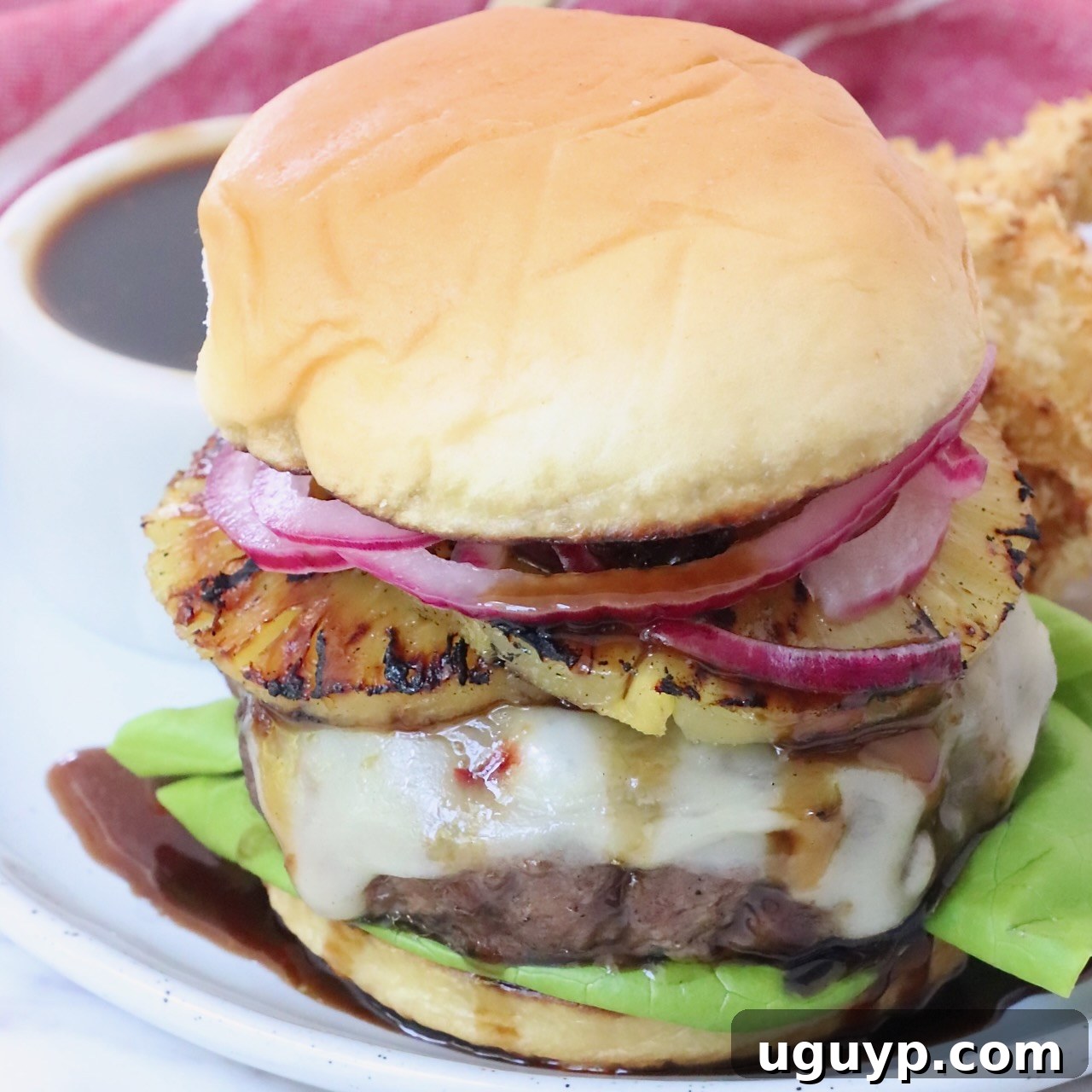 A delicious Hawaiian burger on a plate, topped with grilled pineapple, pepper jack cheese, and teriyaki sauce.