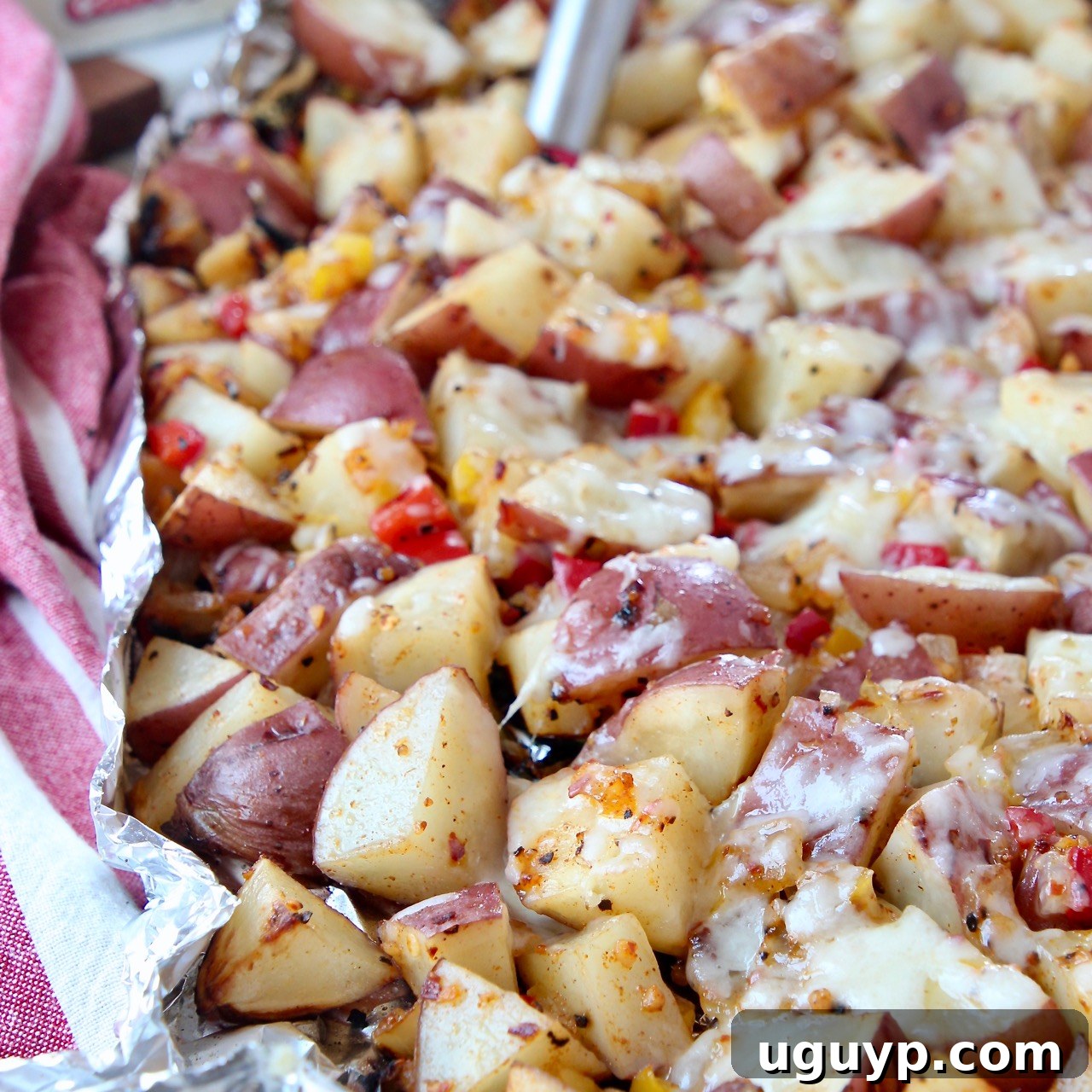 Deliciously cheesy grilled cubed potatoes cooked in foil, being stirred with a spatula, making for a perfect summer side dish.