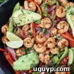shrimp fajitas in a cast iron skillet topped with sliced avocado and lime wedges