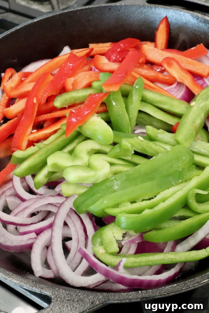 Thinly sliced bell peppers and onions in a hot skillet, beginning to soften.
