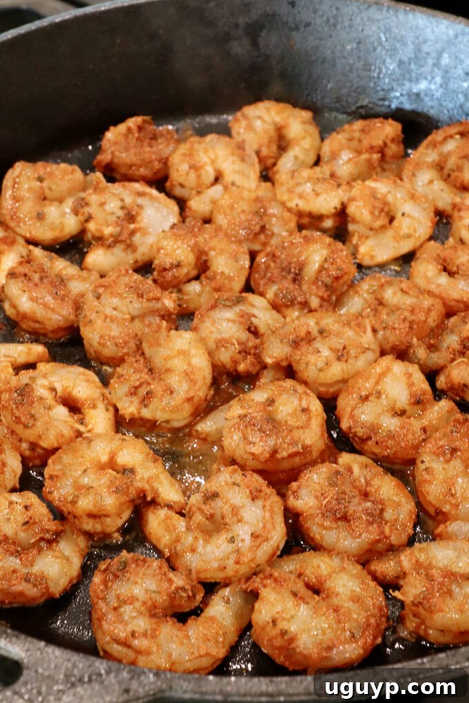Raw, marinated shrimp placed in a hot cast iron skillet, ready to cook.