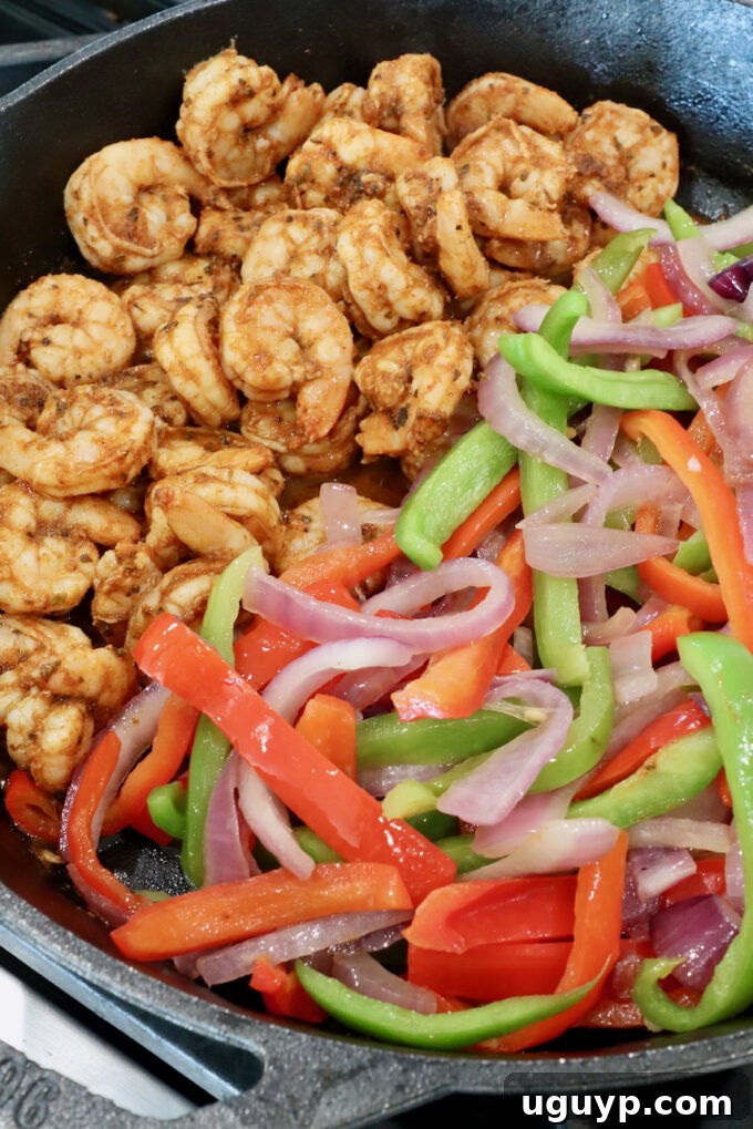 Cooked shrimp combined with sautéed bell peppers and onions in a cast iron skillet.