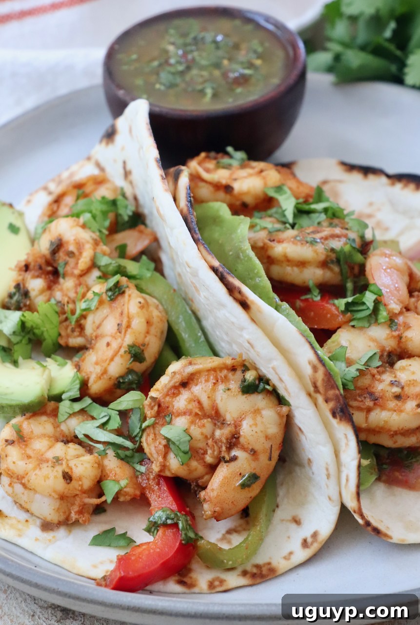 Cooked shrimp fajitas served in tortillas on a plate, garnished with fresh cilantro and avocado.