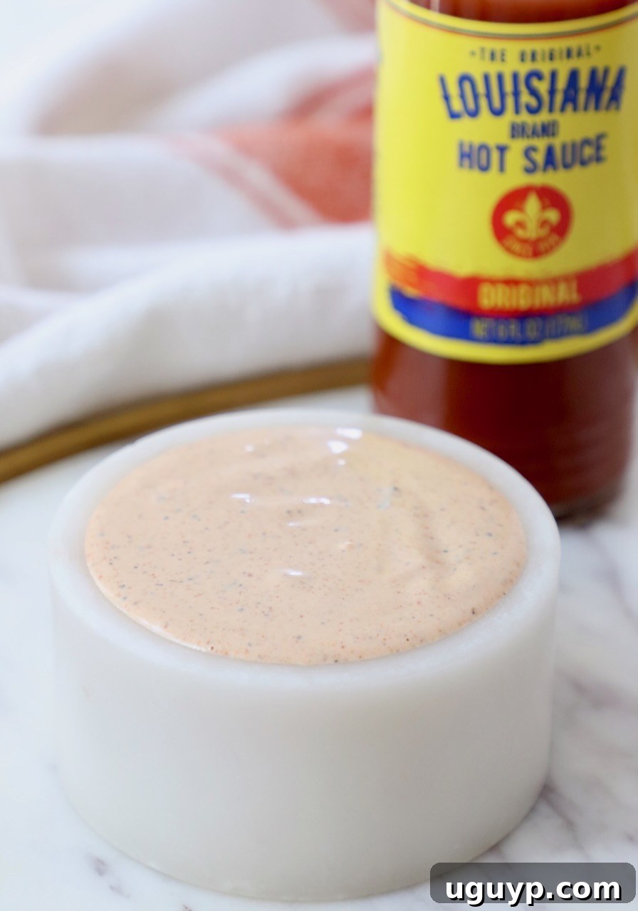 creamy cajun sauce in a small white bowl with a bottle of hot sauce behind it