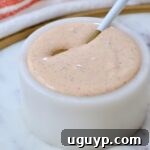 creamy cajun sauce in a small white bowl with a bottle of hot sauce behind it