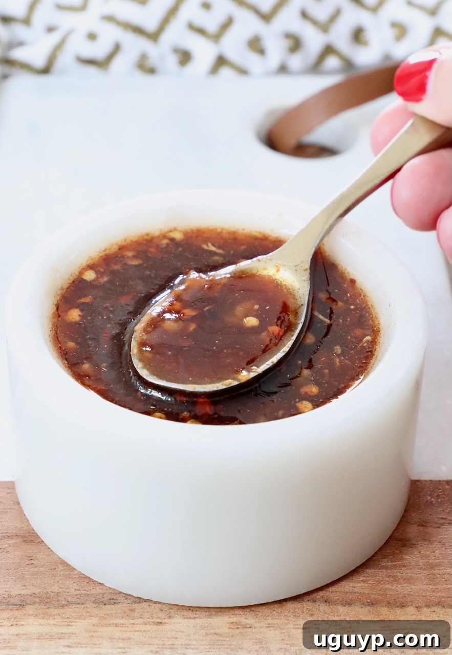 hand holding a spoon dipped into a bowl of sauce