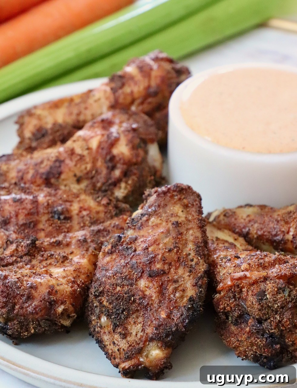A plate of seasoned baked chicken wings, with a small bowl of dipping sauce and a garnish of fresh herbs.