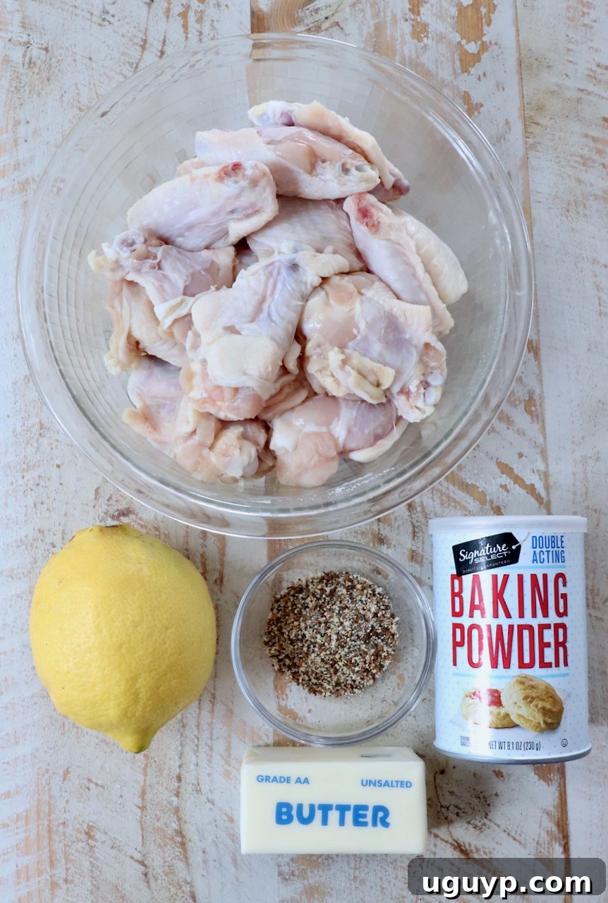 Fresh ingredients for lemon pepper wings, including raw chicken wings, lemon, and spices, laid out on a white wooden board.