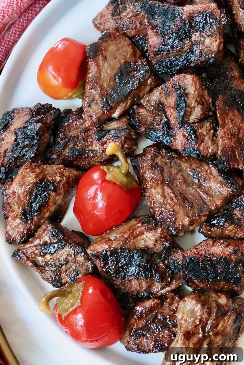 Grilled New England steak tips on a plate with vibrant cherry peppers, ready to be served.