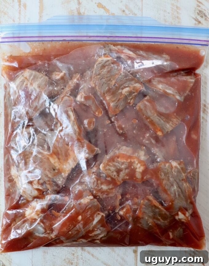 Steak tips soaking in a flavorful marinade inside a large plastic zipper bag.
