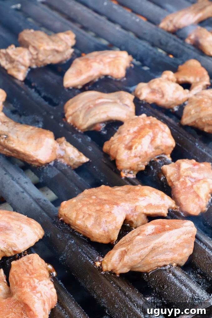 Marinated raw steak tips carefully placed on a hot grill for cooking.