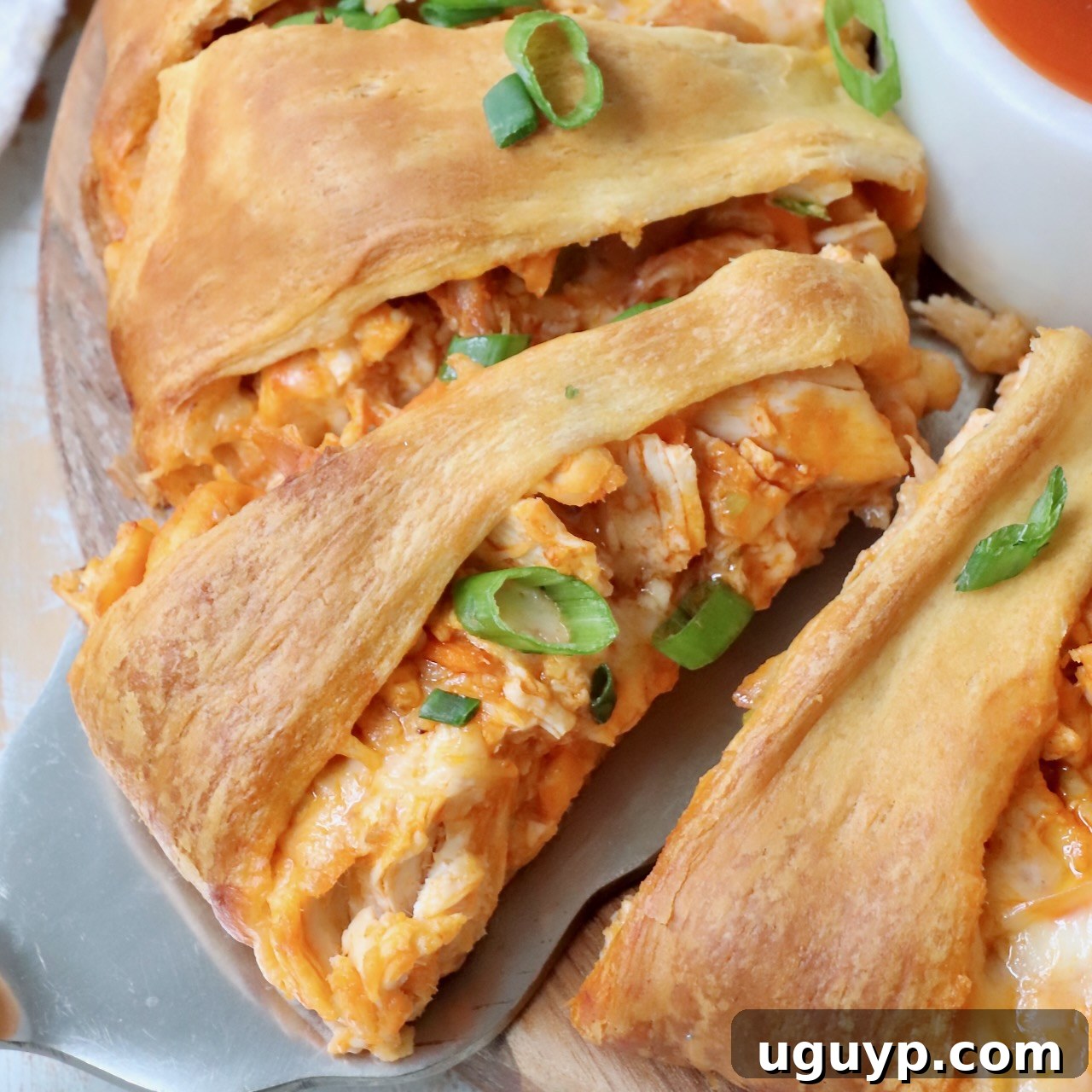 Slice of Buffalo Chicken Crescent Ring on a spatula, showcasing its cheesy filling.