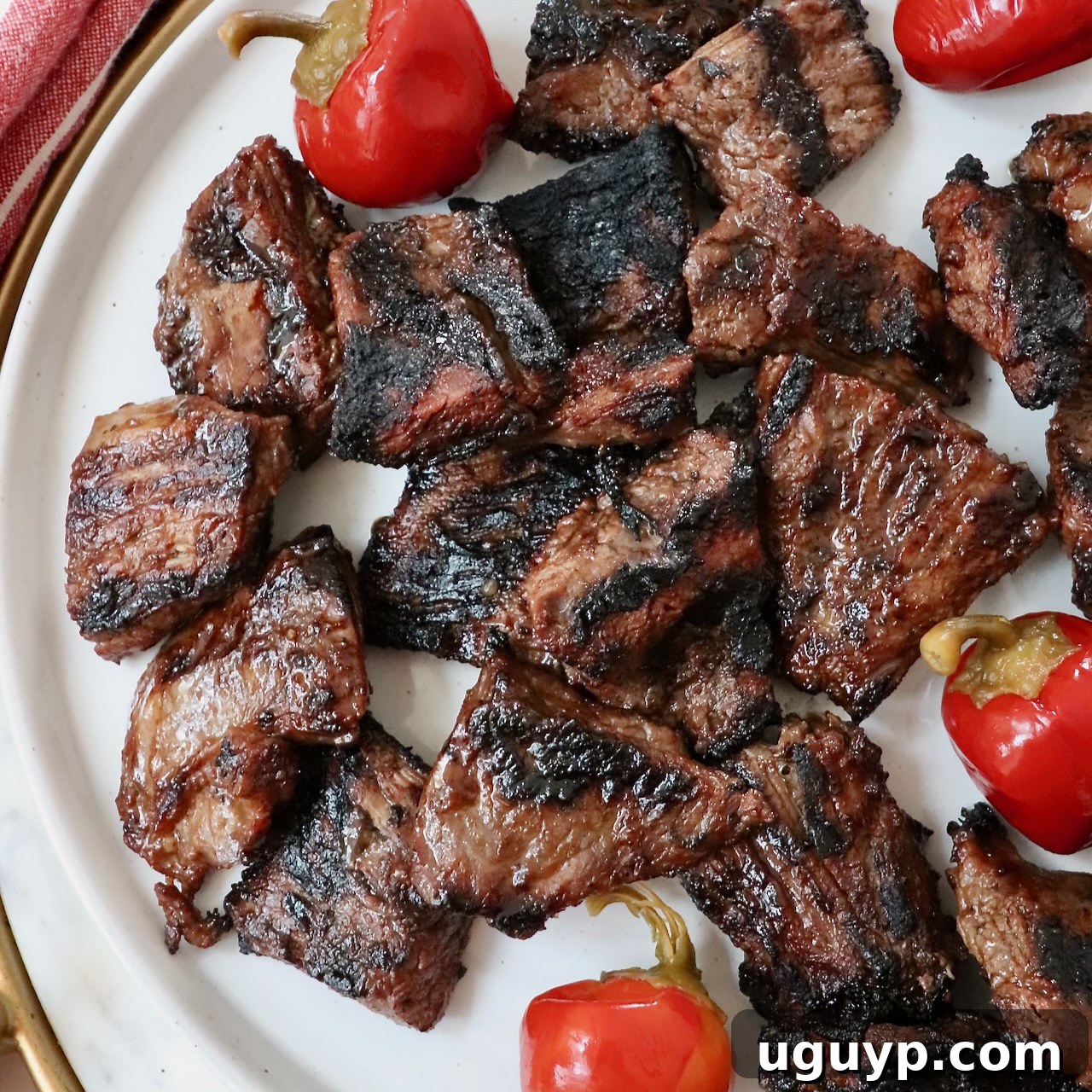 Grilled steak bites on a plate with cherry peppers, perfect for a hearty appetizer.