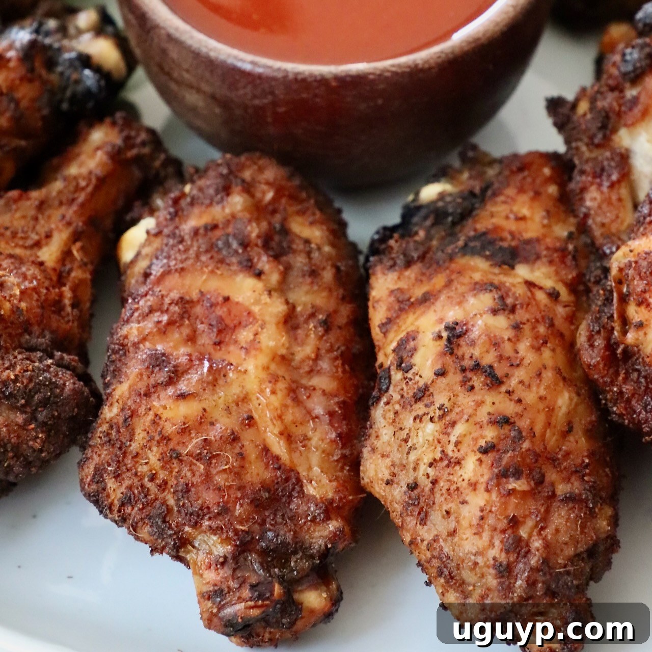 Perfectly baked chicken wings arranged on a plate with a small bowl of buffalo sauce.