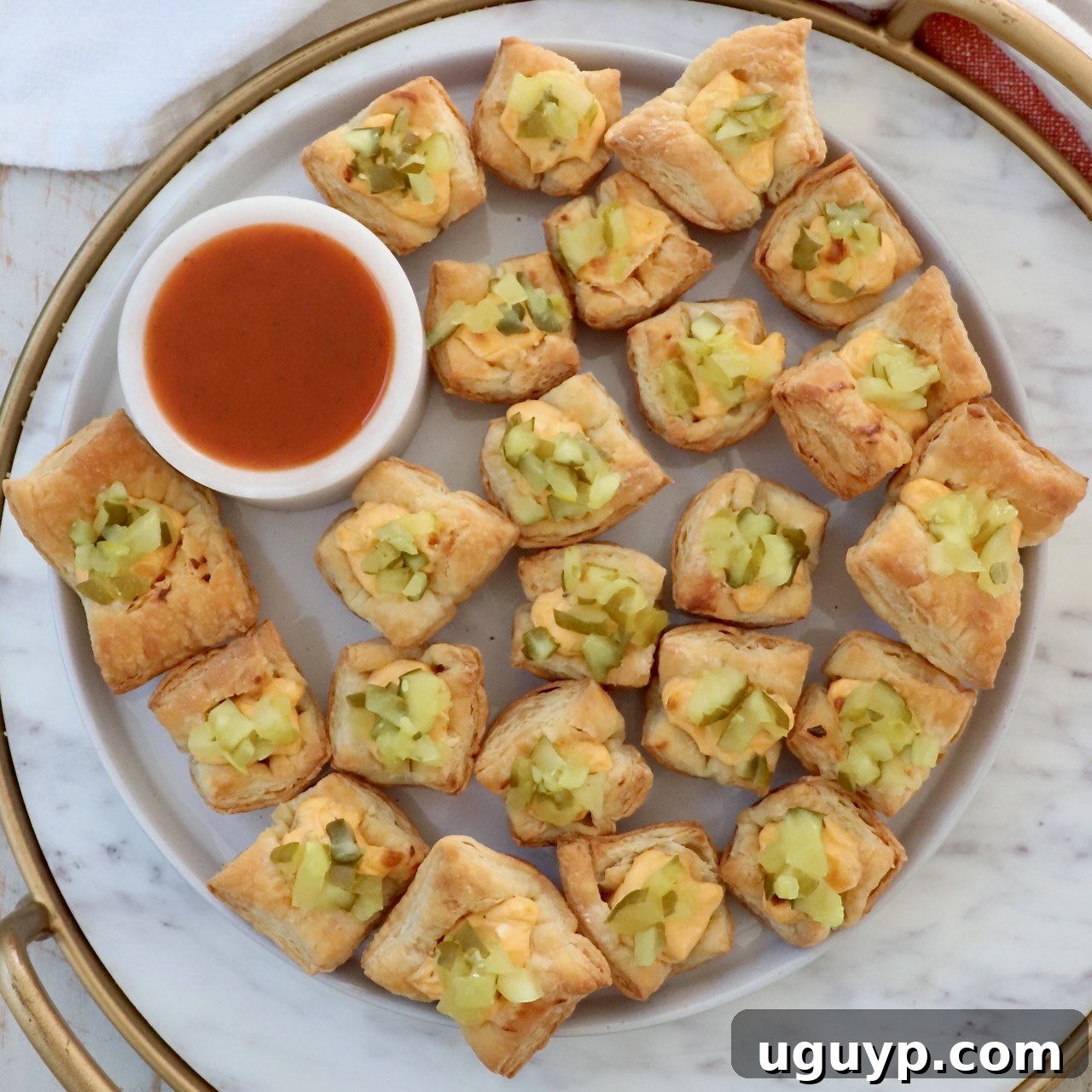 Puff Pastry Pickle Bites on a plate with a small bowl of hot sauce.