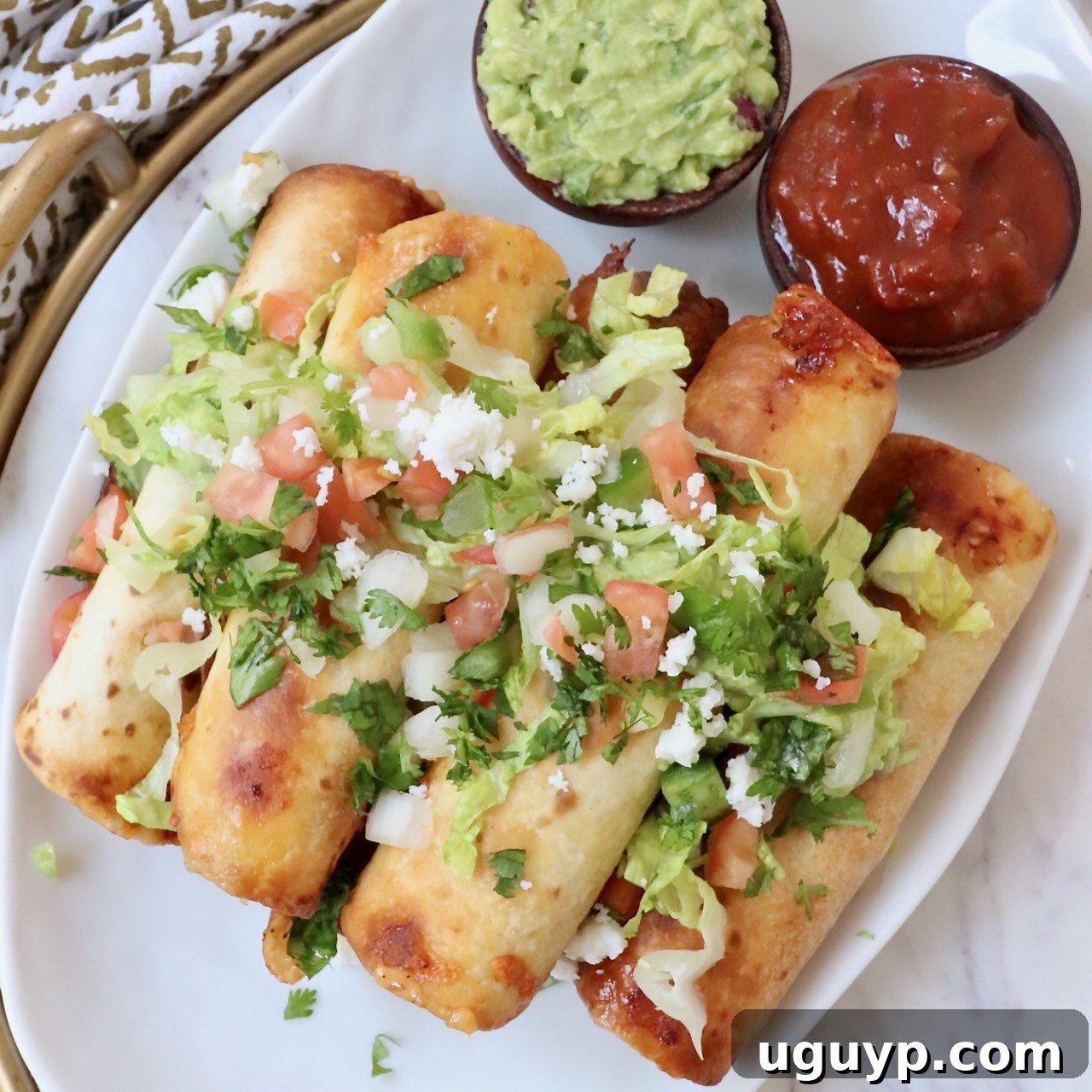 Beef Taquitos stacked on a plate, garnished with guacamole, pico de gallo, and cilantro.