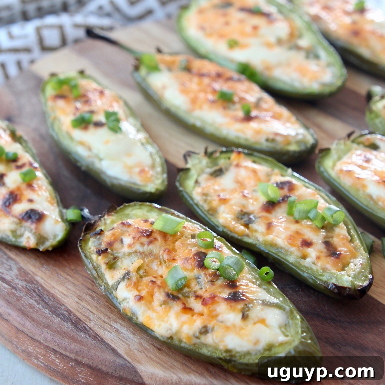 Grilled Jalapeno Poppers on a wooden cutting board, filled with cheese and wrapped in bacon.