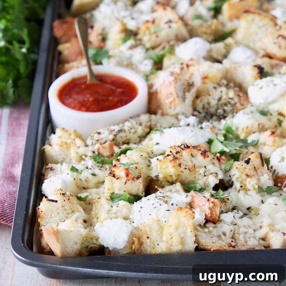 Cubed garlic bread covered in cheese on a baking sheet with a side of marinara sauce.