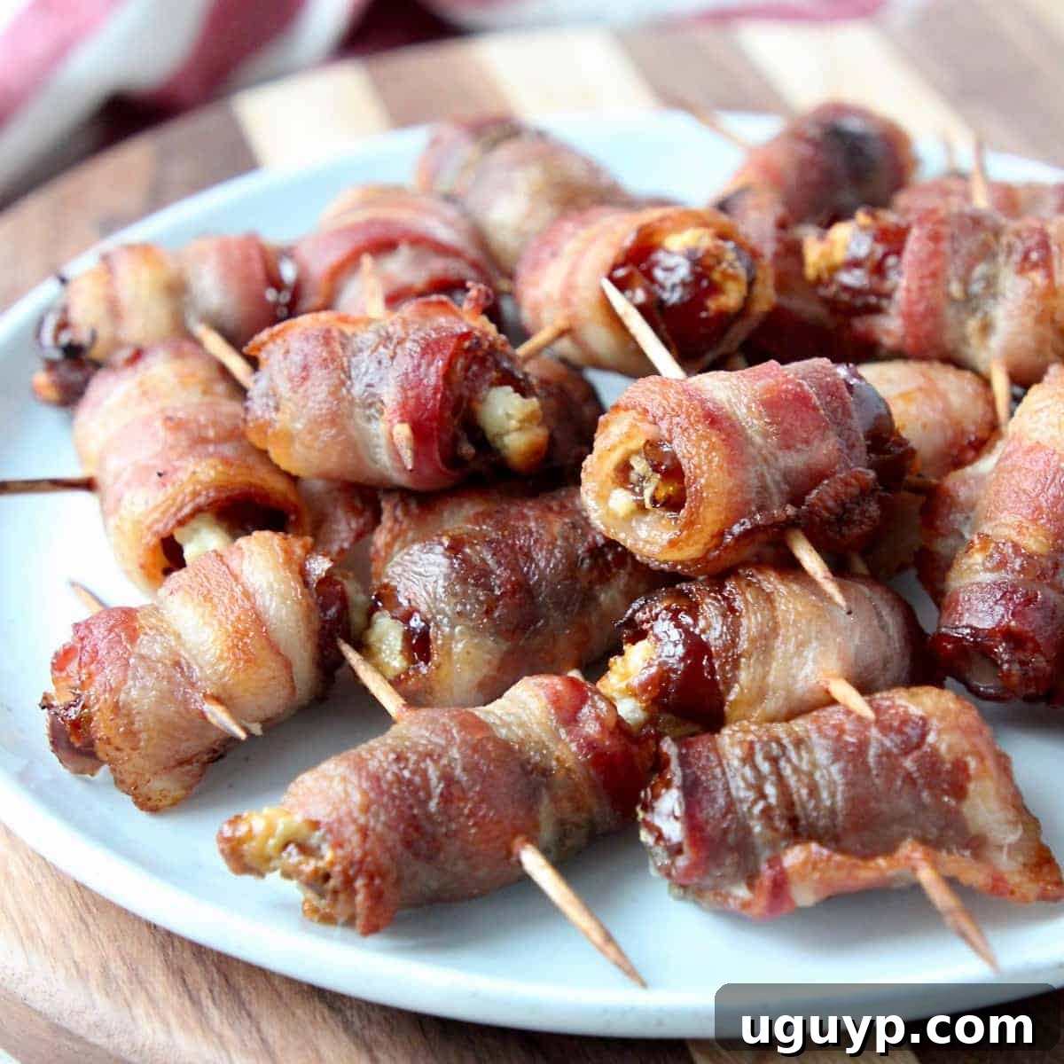 Bacon wrapped dates skewered with toothpicks on a white plate, ready to be served as an appetizer.