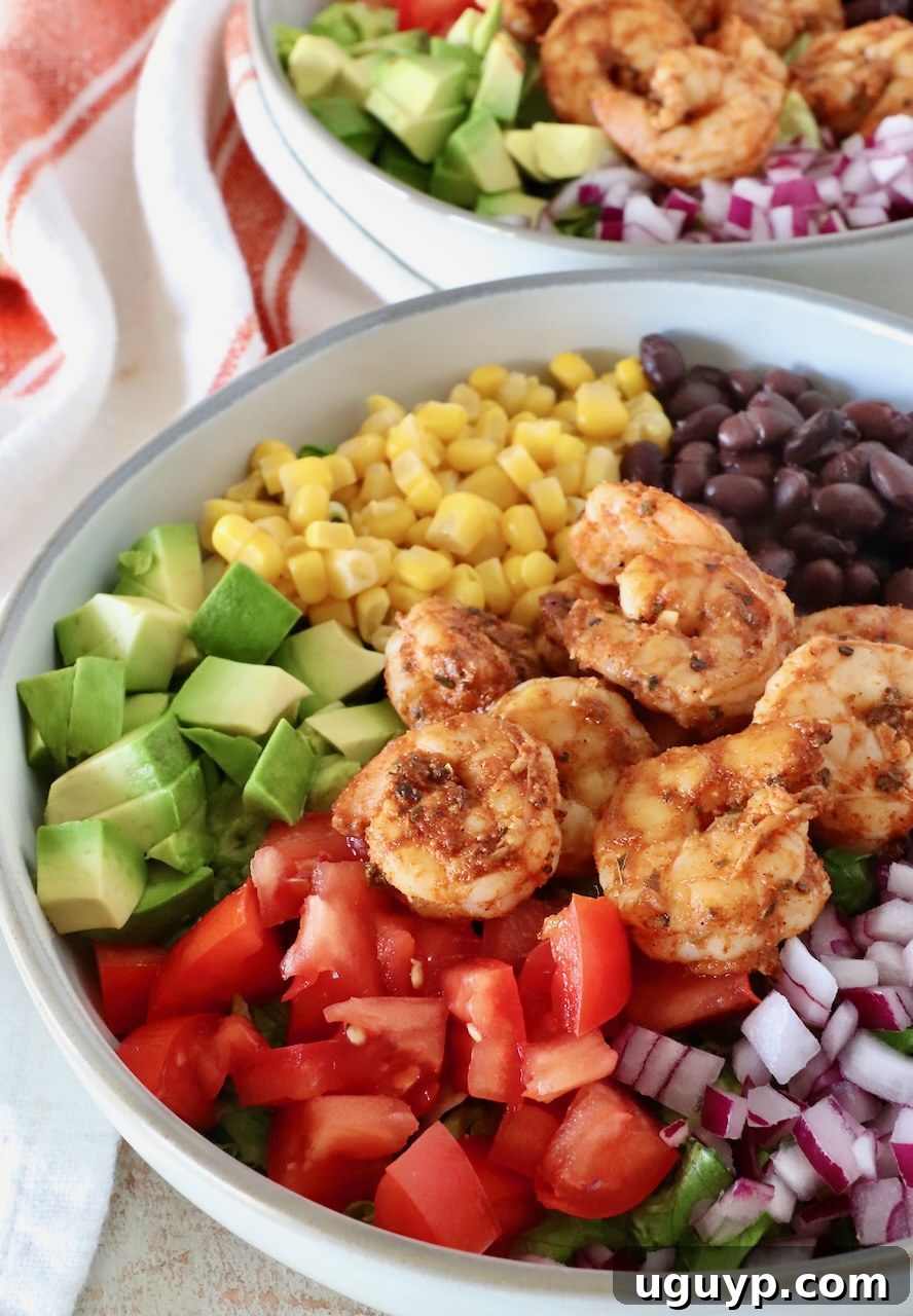 A vibrant Mexican shrimp salad in a bowl, featuring seasoned shrimp, diced avocado, red onions, black beans, corn, and tomatoes over crisp lettuce.