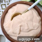 A wooden bowl filled with creamy, light orange sauce. A spoon dips into the smooth mixture.