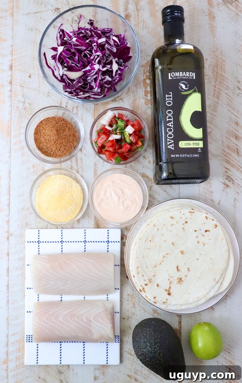 Top-down view of fish taco ingredients on a light wooden surface: red cabbage, avocado oil, taco seasoning, pico de gallo, fish taco sauce, cornmeal, tortillas, fish fillets, avocado, and a lime.