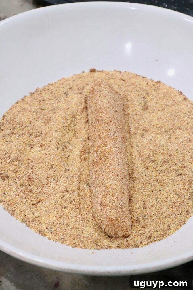 A breaded strip of fish lies on a bed of seasoned cornmeal in a white bowl.